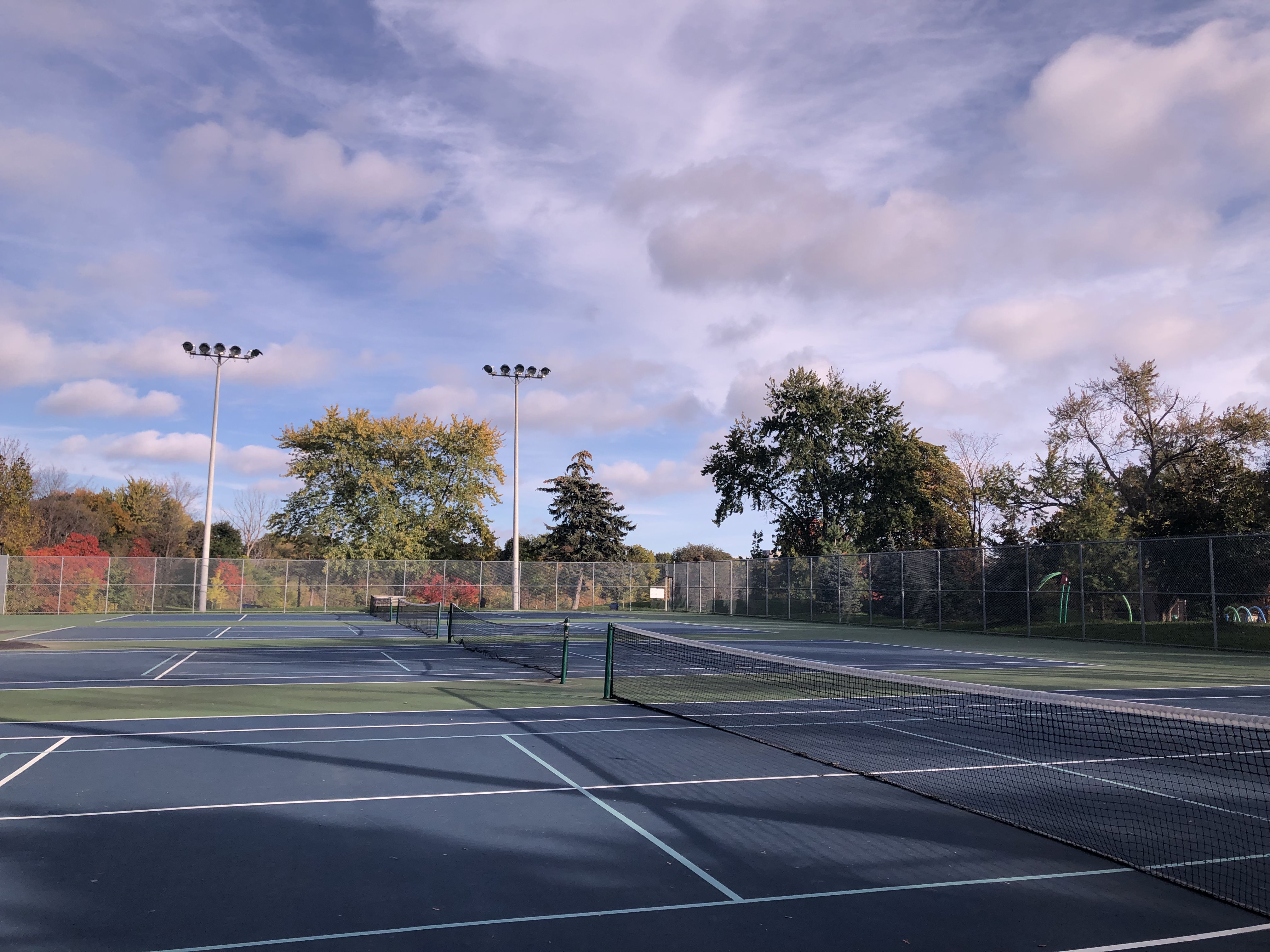 Public outdoor tennis courts at Cedarvale Park in Toronto, with surrounding green space and trees.